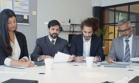 Group of business professionals engaged in a team meeting around a desk in a modern office setting.