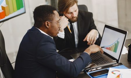Two business professionals working on growth charts using laptop in an office setting.