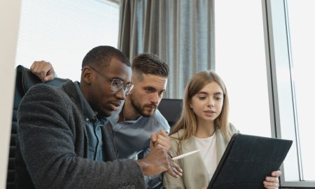 Team of three diverse professionals working on a project with a tablet in a modern office setting.