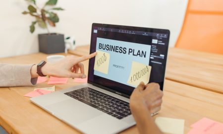 Hands collaborate on a business plan with a laptop in a modern office setting.