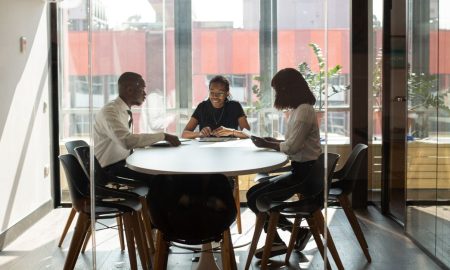 Three professionals collaborating in a modern office boardroom setting during daylight.