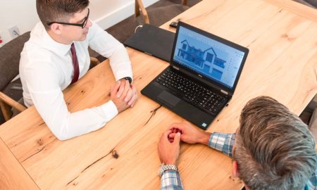 Professionals discuss architectural design on a laptop in a modern office setting.