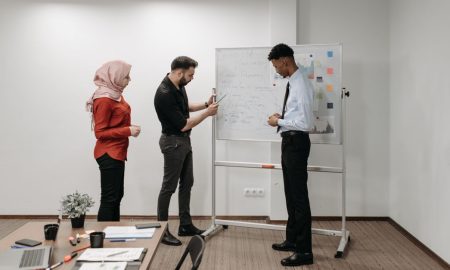 Three professionals discussing project ideas during an office meeting, illustrating teamwork and diversity.