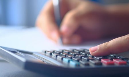 A close-up image of hands working on a calculator and writing, representing budgeting and financial planning.