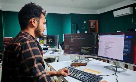 Software developer coding on dual monitors in a well-lit modern office, focused and engaged.