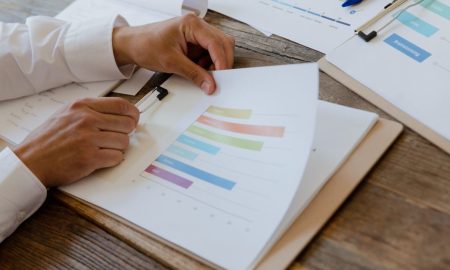 Close-up of hands reviewing business report with colorful charts and graphs on a wooden desk.