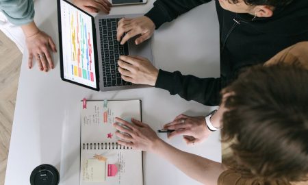 A high-angle view of a team collaborating over a laptop and notebook in a modern office.
