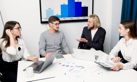 A group of business professionals discussing data at a meeting table with laptops and charts.