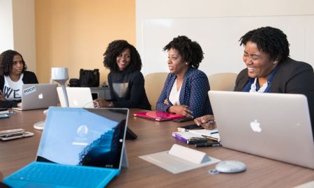 Group of women engaged in a collaborative meeting at an office table with laptops.
