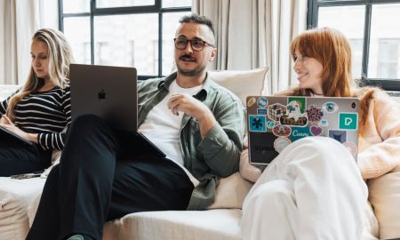 Three adults working on laptops in a casual office environment, discussing ideas.