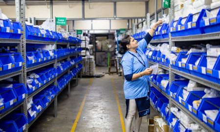 Woman in uniform organizing inventory in a warehouse aisle with labeled bins.