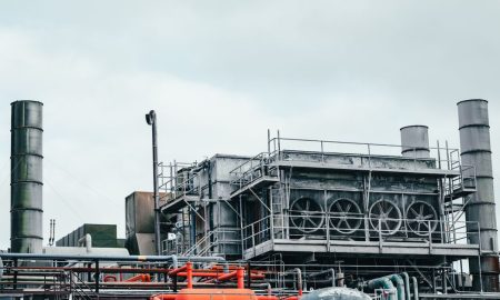 Industrial factory with metal pipes and special equipment surrounded with fences located against cloudy sky on street with power lines in town