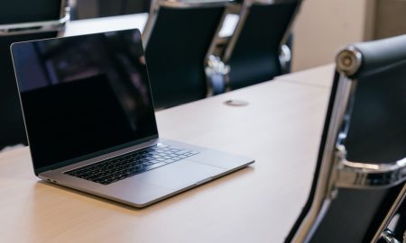 Open laptop on a wooden conference table with stylish black chairs in a modern office setting.