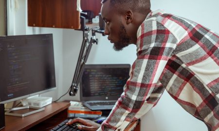 Focused IT specialist in casual attire working at a computer in a modern office setting.