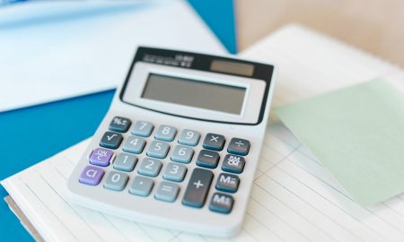 A white calculator on a stack of lined paper with a blue folder, capturing an office setting.