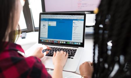 Two women working together on a laptop in a bright, modern office setting.