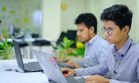 Two young professionals working on laptops in a vibrant and modern office setting.