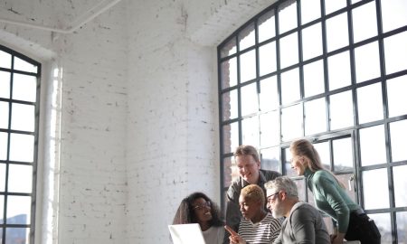 Group of diverse colleagues of different ages discussing business ideas while working on laptop in creative workplace and looking at screen during work
