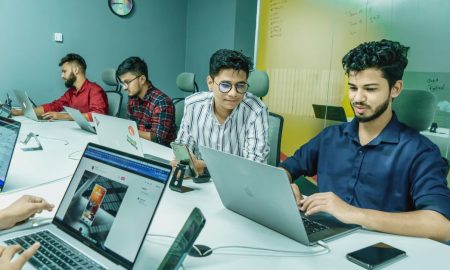Group of young professionals working together in a modern office setting, using laptops and technology.