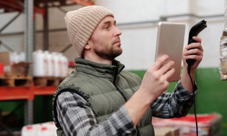 Man in beanie and vest using a scanner in a warehouse for inventory control.
