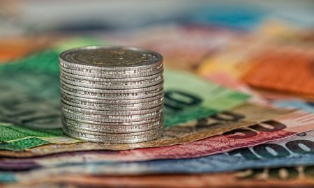 A stack of coins on top of various colored banknotes, symbolizing finance and currency.