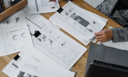 Woman analyzing financial data and reports on a wooden desk with a laptop, showcasing analytics in a workspace.
