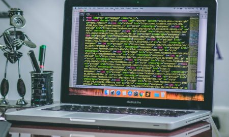 A sleek MacBook Pro displaying code on a desk with office tools and creative decorations.