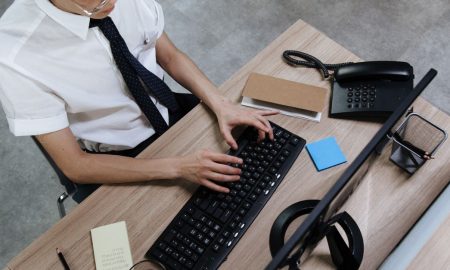 Asian man in business attire typing on a keyboard at a modern office desk.