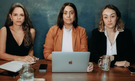 Three serious women in formal wear at a business meeting with laptops and notebooks.