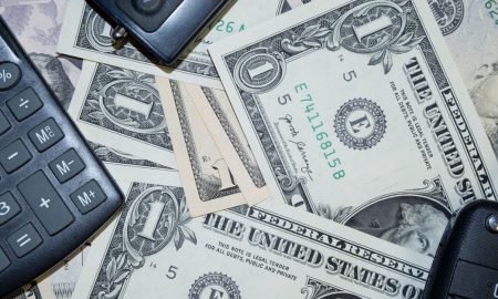An arrangement of US dollar bills, car keys, and a calculator representing finance and investment concepts.
