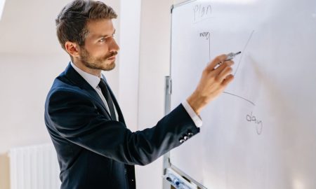 Executive in suit writing on whiteboard, explaining business graph.