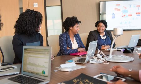 Four diverse women engaged in a business meeting with laptops and presentations in an office.