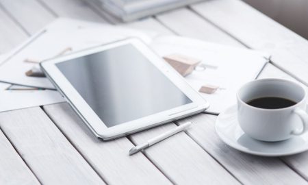 White tablet with stylus and coffee cup on modern office desk setup.
