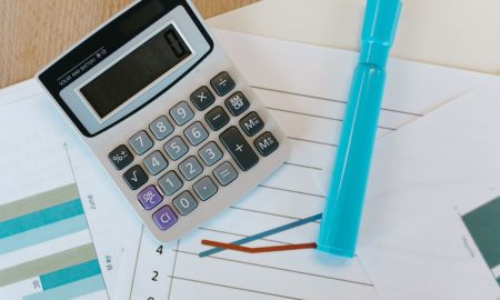 Top view of a calculator and charts on a wooden office desk with a blue marker.