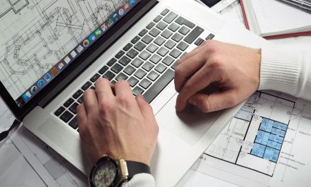 Architect reviewing detailed floor plans and schematics on a laptop with a smartphone nearby.