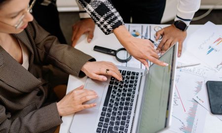 A group of colleagues working together on a laptop amidst documents. Collaborative teamwork in a modern office environment.