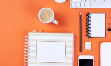 Flat lay of office items on an orange background including keyboard, coffee, and smartphone.