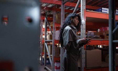An adult woman in uniform checking inventory in a warehouse aisle.