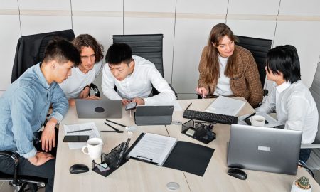A diverse group of colleagues working together in an office setting with laptops and documents.