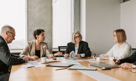Five business professionals engaged in a meeting in a modern office setting, discussing documents and ideas.