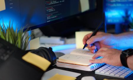A person planning a software project with handwritten notes and code on a monitor in a modern workspace.