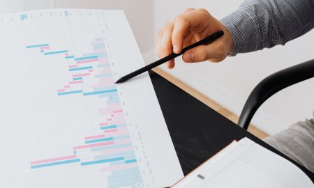Close-up of a person analyzing a colorful graph chart with a pen in a modern office setting.