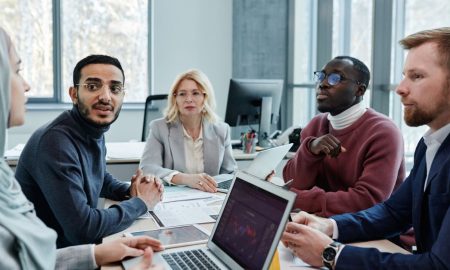 Diverse group of professionals engaged in a conference room discussion with laptops and documents.